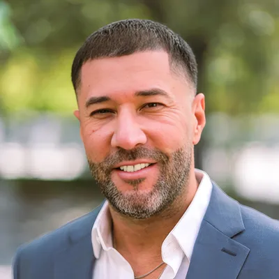 Professional headshot of male executive director in business attire standing inside modern office space.