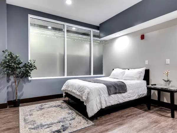 A single neatly made bed with white linens and a grey throw sits in a clean, quiet residential room with a grey accent wall.
