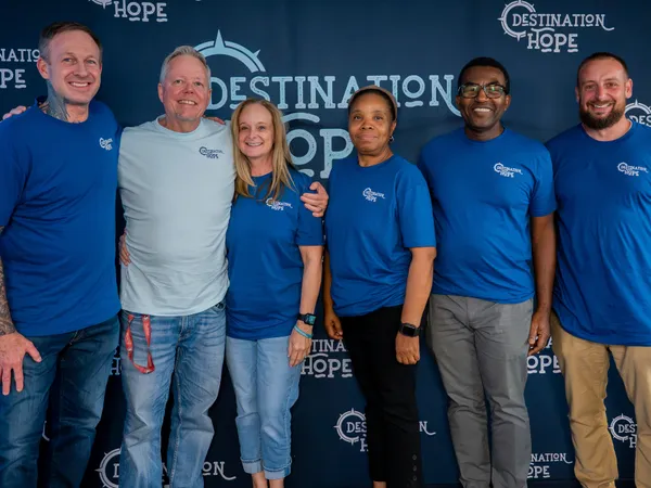 Five smiling staff members standing together in front of the Destination Hope backdrop, showcasing our strong supportive network.