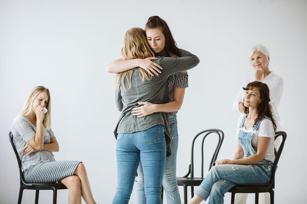 Sad women hugging another woman during a group therapy session about mental health