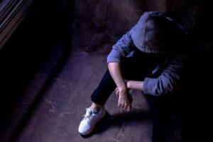 Person in hoodie sitting on the floor hunched over
