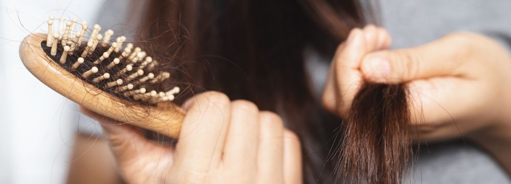 Woman examines hairbrush with stray strands of loose hair due to anxiety